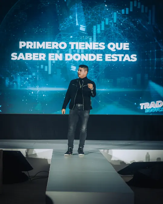 Carlos Valencia dando una conferencia de trading en un escenario, frente a una pantalla con un gráfico